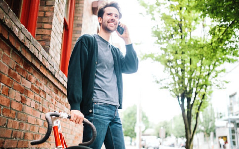 Man on a neighborhood street next to bike talking on his phone and smiling